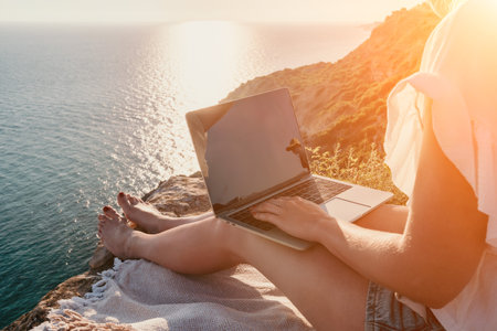 Woman sea laptop. Business woman working on laptop by sea at sunset. Close up on hands of pretty lady typing on computer outdoors summer day. Freelance, digital nomad, travel and holidays concept.の写真素材