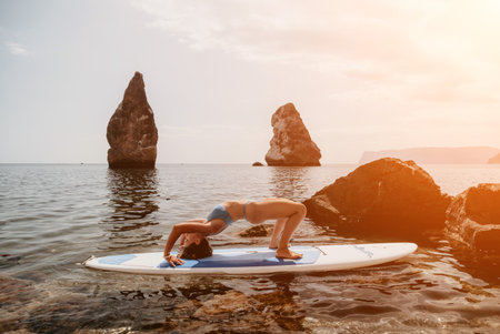 Woman sup yoga. Happy sporty woman practising yoga pilates on paddle sup surfboard. Female stretching doing workout on sea water. Modern individual female hipster outdoor summer sport activity.の写真素材