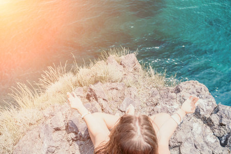 Woman sea yoga. Back view of free calm bliss satisfied woman with long hair standing on top rock with yoga position against of sky by the sea. Healthy lifestyle outdoors in nature, fitness concept.の写真素材
