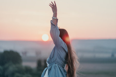 Happy woman standing with her back on the sunset in nature in summer with open hands. Romantic beautiful bride in white boho dress posing with mountains on sunsetの写真素材