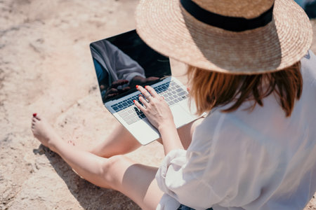 Woman sea laptop. Successful business woman working on laptop by the sea. Pretty lady typing on computer at summer day outdoors. Freelance, digital nomad, travel and holidays concept.の写真素材