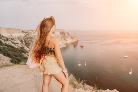 Woman travel sea. Happy tourist taking picture outdoors for memories. Woman traveler looks at the edge of the cliff on the sea bay of mountains, sharing travel adventure journeyの写真素材
