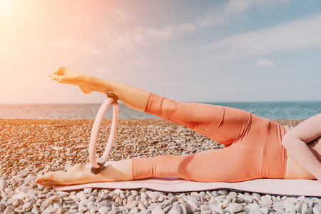 Woman sea pilates. Sporty happy middle aged woman practicing fitness on beach near sea, smiling active female training with ring on yoga mat outside, enjoying healthy lifestyle, harmony and meditationの写真素材