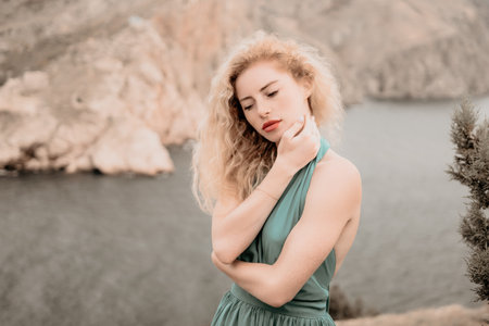 Redhead woman portrait. Curly redhead young caucasian woman with freckles looking at camera and smiling. Close up portrait cute woman in a mint long dress posing on a volcanic rock high above the seaの写真素材