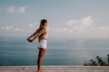Fitness woman sea. A happy middle aged woman in white sportswear exercises morning outdoors in a park with a beach view. Female fitness pilates yoga routine concept. Healthy lifestyle.の写真素材