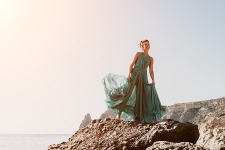 Side view a Young beautiful sensual woman with black hair in a long mint dress posing on a beach with calm sea bokeh lights on sunny day. Girl on the nature on blue sky background. Fashion photoの写真素材