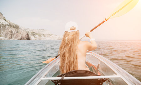 Woman in kayak back view. Happy young woman with long hair floating in transparent kayak on the crystal clear sea. Summer holiday vacation and cheerful female people relaxing having fun on the boatの写真素材