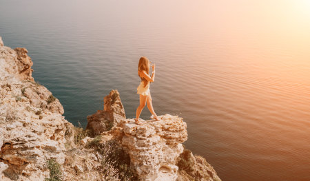 Woman travel sea. Happy tourist enjoy taking picture outdoors for memories. Woman traveler looks at the edge of the cliff on the sea bay of mountains, sharing travel adventure journeyの写真素材