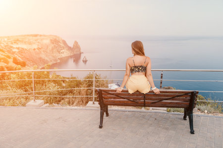 Woman travel sea. Happy tourist enjoy taking picture outdoors for memories. Woman traveler looks at the edge of the cliff on the sea bay of mountains, sharing travel adventure journeyの写真素材