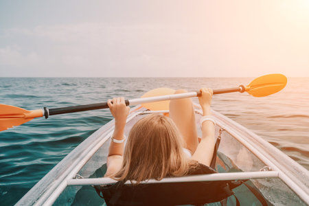 Woman in kayak back view. Happy young woman with long hair floating in transparent kayak on the crystal clear sea. Summer holiday vacation and cheerful female people relaxing having fun on the boatの写真素材