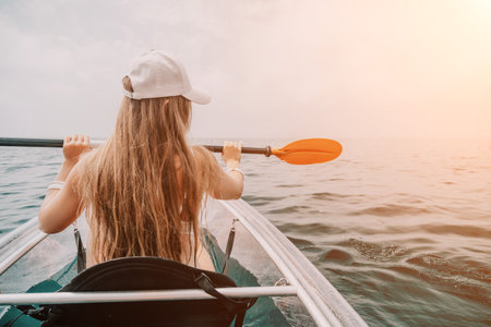 Woman in kayak back view. Happy young woman with long hair floating in transparent kayak on the crystal clear sea. Summer holiday vacation and cheerful female people relaxing having fun on the boatの写真素材