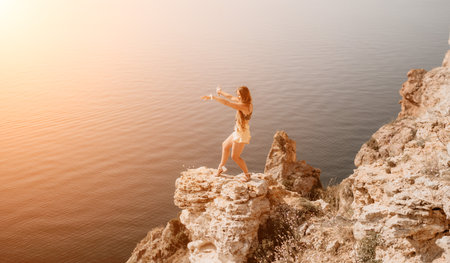 Woman travel sea. Happy tourist enjoy taking picture outdoors for memories. Woman traveler looks at the edge of the cliff on the sea bay of mountains, sharing travel adventure journeyの写真素材