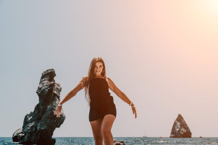 Woman summer travel sea. Happy tourist in hat enjoy taking picture outdoors for memories. Woman traveler posing on the beach at sea surrounded by volcanic mountains, sharing travel adventure journeyの写真素材