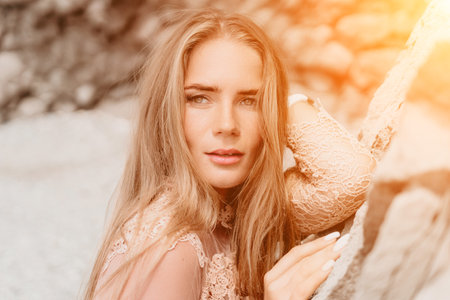 Woman summer travel sea. Happy tourist in beige dress enjoy taking picture outdoors for memories. Woman traveler posing on the beach surrounded by volcanic mountains, sharing travel adventure journeyの写真素材