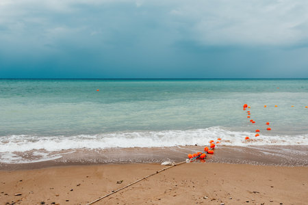Overcast sky on rainy day with foamy waves rolling towards golden sand beach under low warm sun light. Nobody. Holiday recreation concept. Abstract nautical summer ocean sunset nature.の写真素材