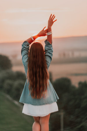 Happy woman standing with her back on the sunset in nature in summer with open hands. Romantic beautiful bride in white boho dress posing with mountains on sunsetの写真素材