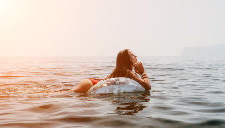 Woman summer sea. Happy woman swimming with inflatable donut on the beach in summer sunny day, surrounded by volcanic mountains. Summer vacation concept.の写真素材