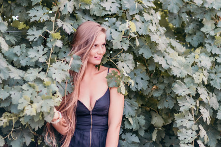 Woman travel winery. Portrait of happy woman holding glass of wine and enjoying in vineyard. Elegant young lady in hat toasting with wineglass smiling cheerfully enjoying her stay at vineyard.の写真素材