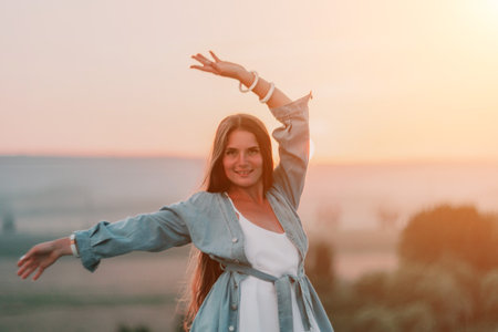 Happy woman standing with her back on the sunset in nature in summer with open hands. Romantic beautiful bride in white boho dress posing with mountains on sunsetの写真素材