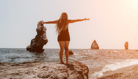 Woman summer travel sea. Happy tourist in hat enjoy taking picture outdoors for memories. Woman traveler posing on the beach at sea surrounded by volcanic mountains, sharing travel adventure journeyの写真素材