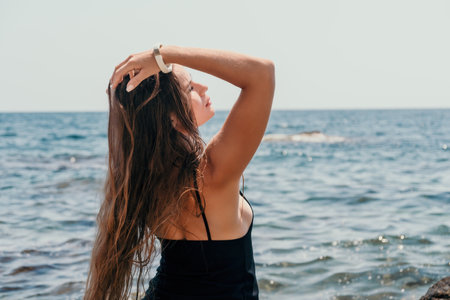 Woman summer travel sea. Happy tourist in hat enjoy taking picture outdoors for memories. Woman traveler posing on the beach at sea surrounded by volcanic mountains, sharing travel adventure journeyの写真素材