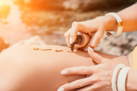 Suntan Lotion. Sexy Woman in bikini apply sun protection cream on her smooth tanned legs. Skin care. Legs on the beach. Close up of female legs with smearing moisturizing lotion. Sunblock concept.の写真素材
