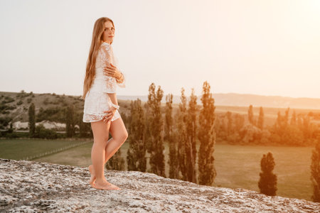 Happy woman in white boho dress on sunset in mountains. Romantic woman with long hair standing with her back on the sunset in nature in summer with open hands. Silhouette. Nature. Sunset.の写真素材