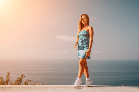 Woman travel sea. Happy tourist in blue dress takes a photo outdoors to capture memories. woman traveling and enjoying her surroundings on the beach, with volcanic mountains in the background.の写真素材