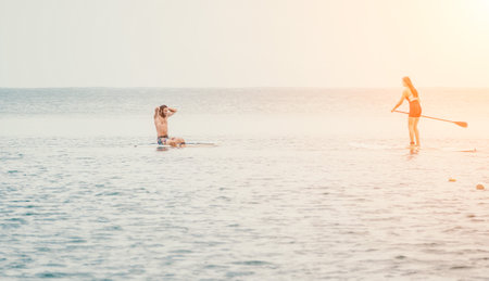 Sea woman and man on sup. Silhouette of happy young woman and man, surfing on SUP board, confident...
