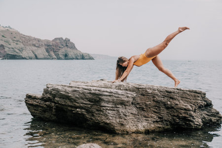 Woman sea yoga. Back view of free calm bliss satisfied woman with long hair standing on top rock with yoga position against of sky by the sea. Healthy lifestyle outdoors in nature, fitness concept.の写真素材
