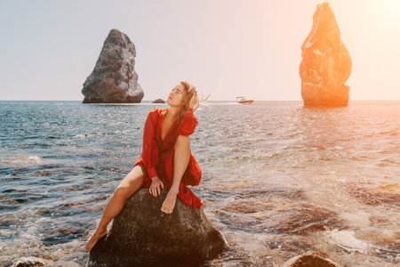 Woman summer travel sea. Happy tourist in long red dress enjoy taking picture outdoors for memories. Woman traveler posing on beach at sea surrounded by volcanic mountains, sharing travel adventureの写真素材