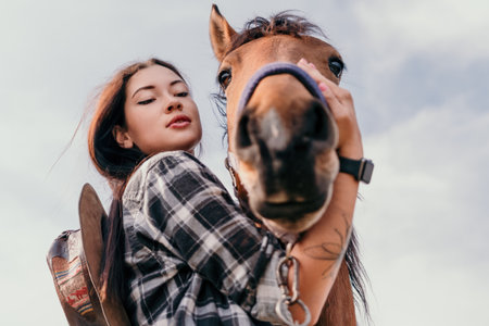 Young happy woman in hat with her horse in evening sunset light. Outdoor photography with fashion model girl. Lifestyle mood. Concept of outdoor riding, sports and recreation.の写真素材