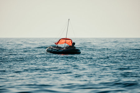 Fisher sea boat. Tourist maneuvering an inflatable boat while fishing in a life jacket, with the beautiful sunset sea in the background. a relaxing fishing trip.の写真素材