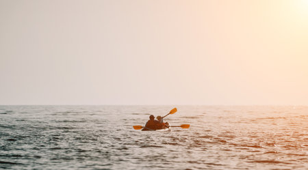 Happy couple kayaks in an inflatable kayak on the sea at sunset. Couple kanoeing in the sea near the island with mountains. People kayaking in life jackets sail. Back viewの写真素材