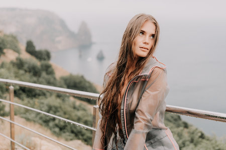 Woman rain umbrella. Happy woman portrait wearing a raincoat with transparent umbrella outdoors on rainy day in park near sea. Girl on the nature on rainy overcast day.の写真素材