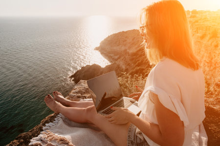 Woman sea laptop. Business woman working on laptop by sea at sunset. Close up on hands of pretty lady typing on computer outdoors summer day. Freelance, digital nomad, travel and holidays concept.の写真素材