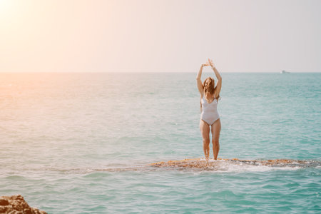 Woman sea yoga. Back view of free calm happy satisfied woman with long hair standing on top rock with yoga position against of sky by the sea. Healthy lifestyle outdoors in nature, fitness conceptの写真素材