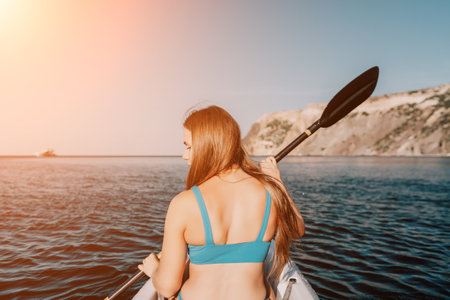 Woman in kayak back view. Happy young woman with long hair floating in kayak on calm sea. Summer holiday vacation and cheerful female people relaxing having fun on the boat.の写真素材