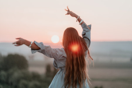 Happy woman standing with her back on the sunset in nature in summer with open hands. Romantic beautiful bride in white boho dress posing with mountains on sunsetの写真素材
