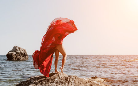 Woman travel sea. Happy tourist in long red dress enjoy taking picture outdoors for memories. Woman traveler posing on beach at sea surrounded by volcanic mountains, sharing travel adventure journeyの写真素材
