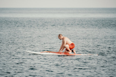 Active mature male paddler with his paddleboard and paddle on a sea at summer. Happy senior man stands with a SUP board. Stand up paddle boarding - outdor active recreation in nature.の写真素材