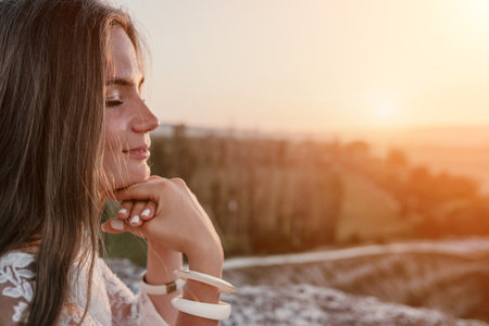 Happy woman in white boho dress on sunset in mountains. Romantic woman with long hair standing with her back on the sunset in nature in summer with open hands. Silhouette. Nature. Sunset.の写真素材