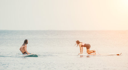 Sea woman and man on sup. Silhouette of happy young woman and man, surfing on SUP board, confident paddling through water surface. Idyllic sunset. Active lifestyle at sea or river.の写真素材
