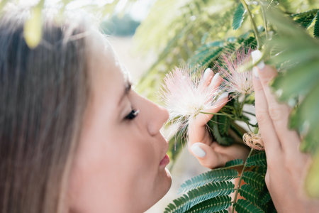 Beauty portrait of happy woman closeup. Young girl smelling Chinese acacia pink blossoming flowers. Portrait of young woman in blooming spring, summer garden. Romantic vibe. Female and natureの写真素材