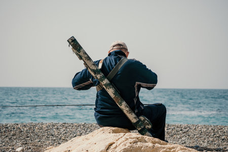 Man hobby fishing on sea tightens a fishing line reel of fish summer. Calm surface sea. Close-up of a fisherman hands twist reel with fishing line on a rod. Fishing in the sea outdoors. Slow motion.の写真素材