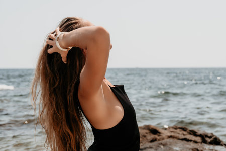 Woman summer travel sea. Happy tourist in hat enjoy taking picture outdoors for memories. Woman traveler posing on the beach at sea surrounded by volcanic mountains, sharing travel adventure journeyの写真素材