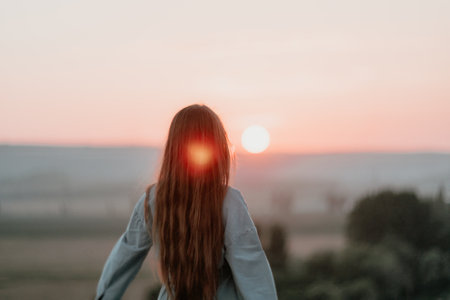 Happy woman standing with her back on the sunset in nature in summer with open hands. Romantic beautiful bride in white boho dress posing with mountains on sunsetの写真素材