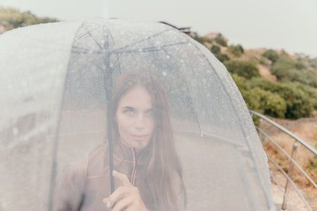 Woman rain umbrella. Happy woman portrait wearing a raincoat with transparent umbrella outdoors on rainy day in park near sea. Girl on the nature on rainy overcast day.の写真素材