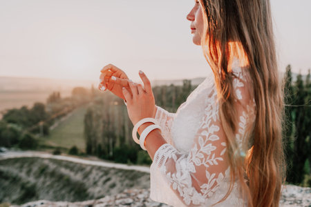 Happy woman in white boho dress on sunset in mountains. Romantic woman with long hair standing with her back on the sunset in nature in summer with open hands. Silhouette. Nature. Sunset.の写真素材