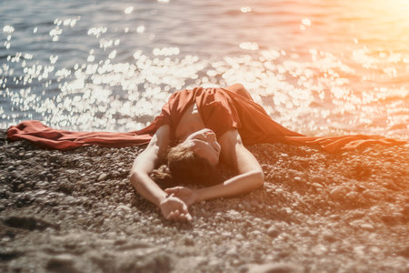 Woman in red dress on sea. Side view a Young beautiful sensual woman in a red long dress posing on the beach near sea on sunset. Girl on the nature on blue sky background. Fashion photo.の写真素材